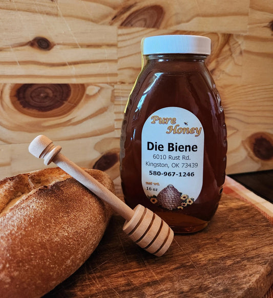Honey bottle with a wooden dipper on a wooden surface, featuring 'Pure Honey Die Biene' branding.